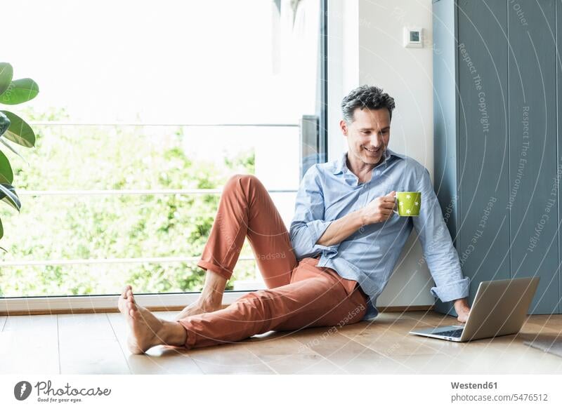 Mature man relaxing at home with a cup of coffee, using laptop windows computers Laptop Computer Laptop Computers laptops notebook smile Seated sit drink
