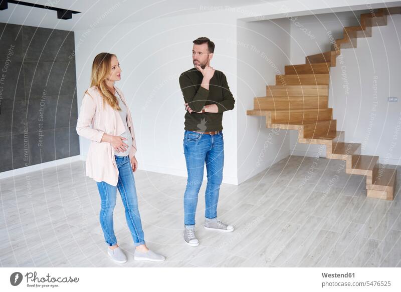 Couple standing in empty flat looking around looking round look round look around couple twosomes partnership couples emptiness flats apartment apartments view