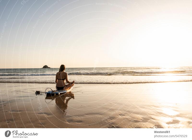 Young woman practicing yoga on the beach, sitting on surfboard, meditating Sea ocean young women young woman cross-legged tailor seat practice practise exercise