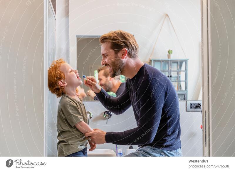 Happy man brushing son's teeth with toothbrush in bathroom at home color image colour image indoors indoor shot indoor shots interior interior view Interiors