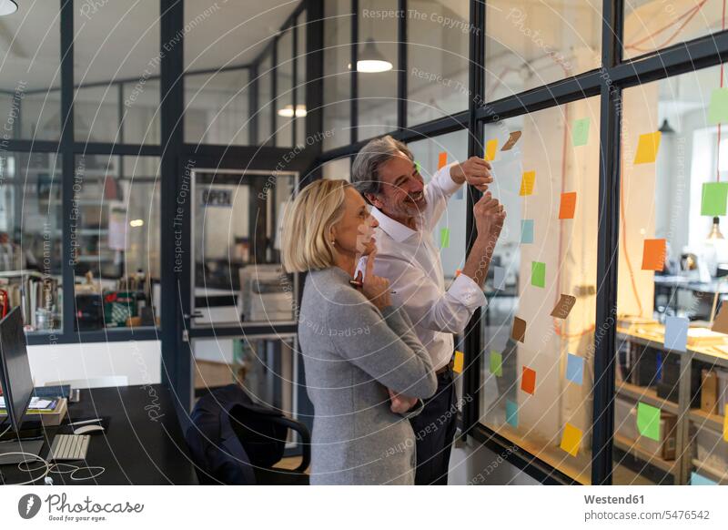 Happy colleagues looking at sticky notes at glass pane in office human human being human beings humans person persons caucasian appearance caucasian ethnicity