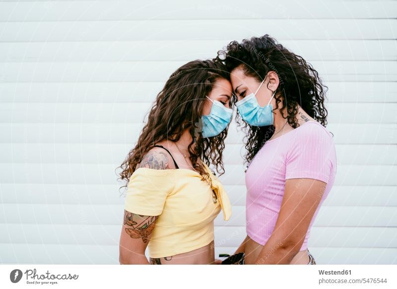 Lesbian couple wearing masks with face to face standing against wall in city color image colour image Spain leisure activity leisure activities free time
