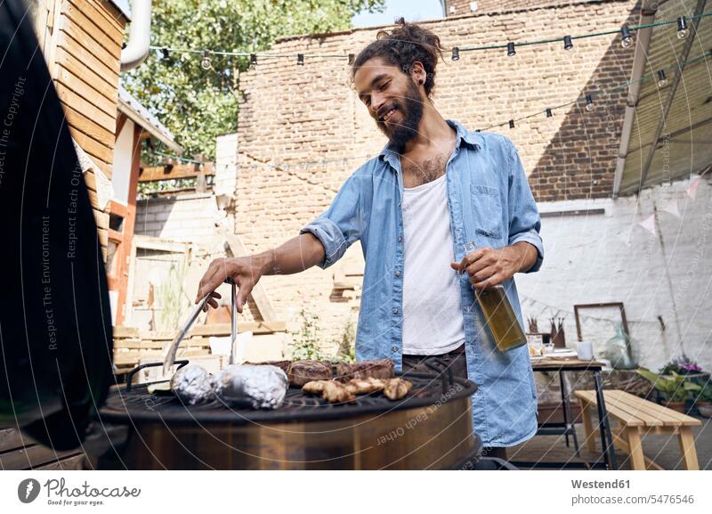 Young man preparing meat on a barbecue grill in a backyard Party Parties Barbecue BBQ Barbeque Beer Beers Ale drinking Food Preparation preparing food cooking