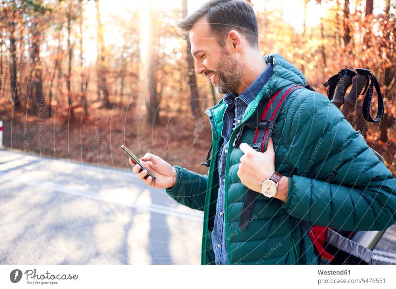 Smiling man checking smartphone on a road in the woods during backpacking trip Smartphone iPhone Smartphones rucksacks backpacks back-packs streets roads