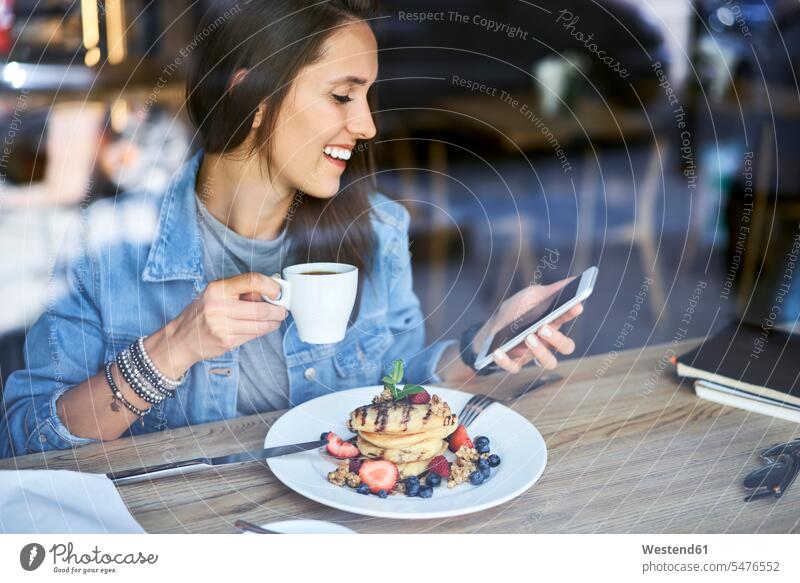 Smiling young woman with plate of pancakes using phone in cafe smiling smile mobile phone mobiles mobile phones Cellphone cell phone cell phones Plate dish