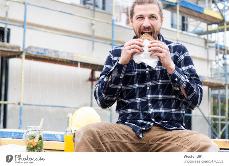 Construction worker eating bread while sitting against building at construction site color image colour image Germany Architecture Building Site Building Sites