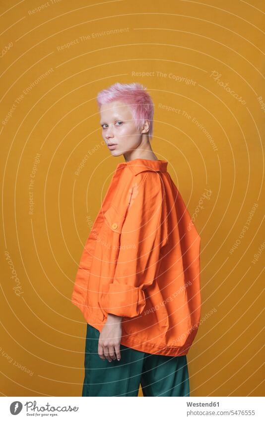 Portrait of young woman with short pink hair wearing orange jacket in front of yellow background human human being human beings humans person persons punks coat