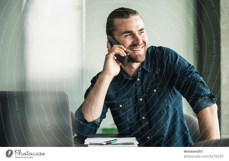 Smiling young businessman on cell phone in office smiling smile Businessman Business man Businessmen Business men offices office room office rooms mobile phone