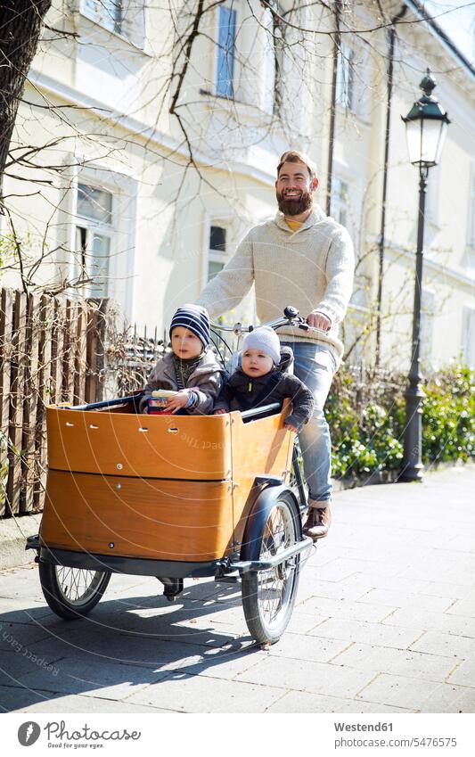Happy father with two children riding cargo bike in the city babies infants baby happiness happy bicycle bikes bicycles cargo bicycle pa fathers daddy dads papa