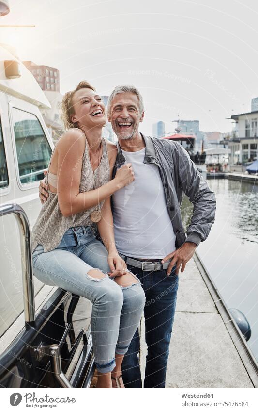 Laughing older man and young woman standing on jetty next to yacht laughing Laughter jetties Yacht Yachts couple twosomes partnership couples positive Emotion