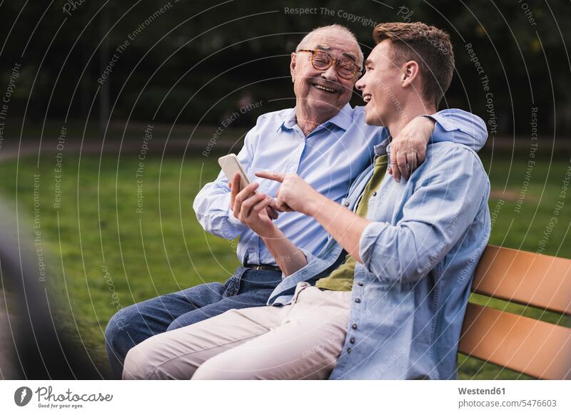 Senior man and grandson with smartphone sitting together on a park bench having fun generation benches park benches phones telephone telephones cell phone