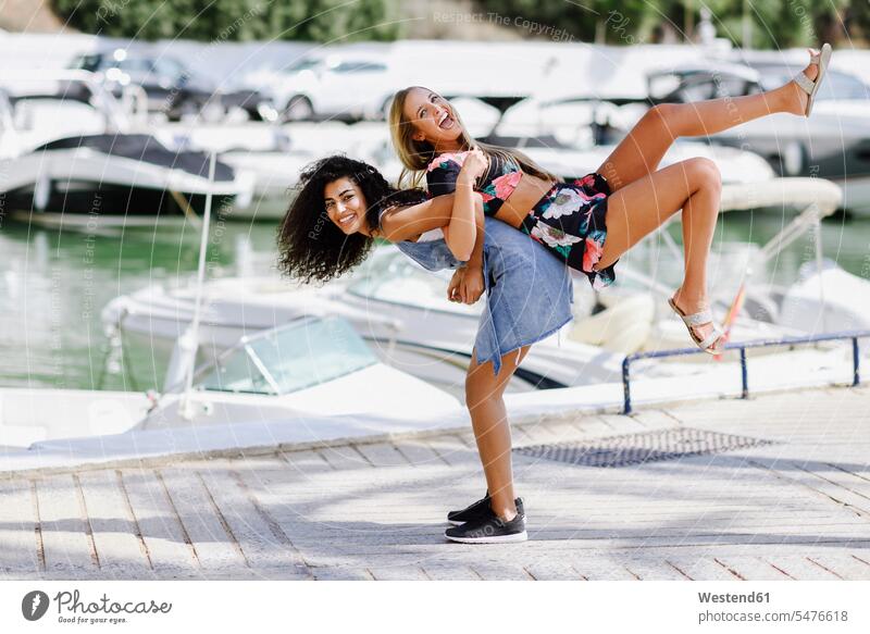 Two playful young women at waterfront promenade in summer promenades female friends woman females summer time summery summertime laughing Laughter mate