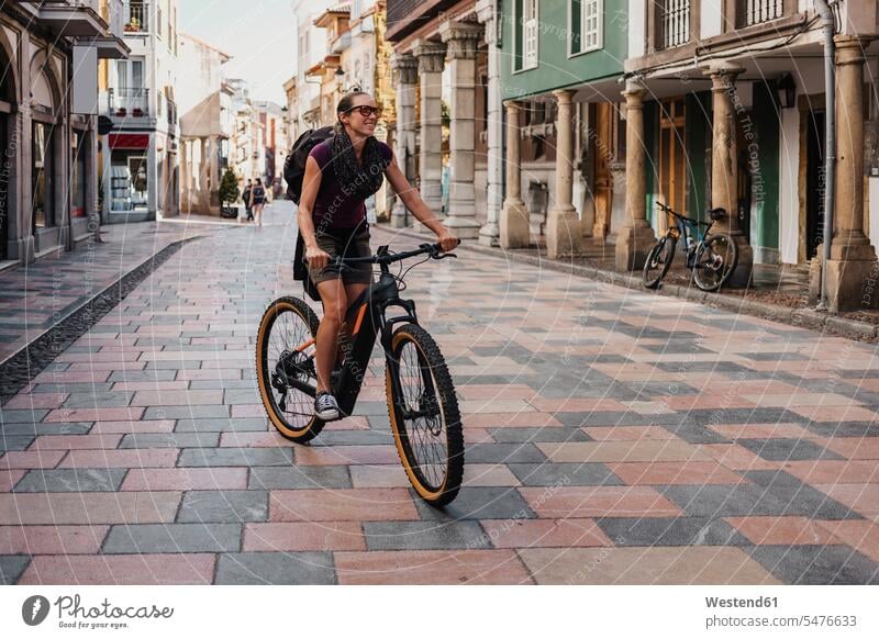 Woman with backpack riding electric mountain bike on street in city color image colour image outdoors location shots outdoor shot outdoor shots day