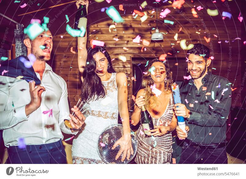 Male and female friends with champagne and disco ball dancing amidst confetti in party color image colour image indoors indoor shot indoor shots interior