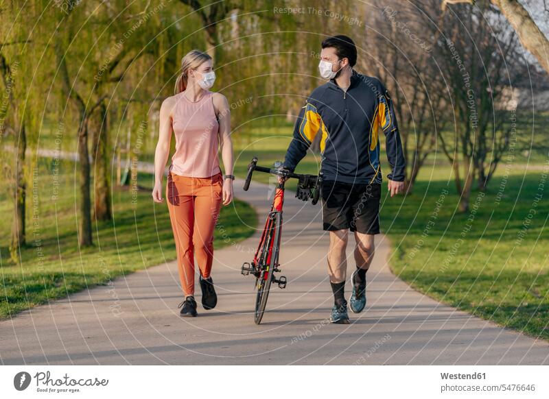 Young couple walking with bicycle on footpath at park during coronavirus pandemic color image colour image outdoors location shots outdoor shot outdoor shots
