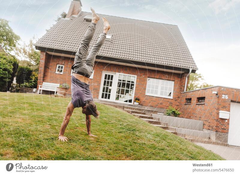 Mature man doing a handstand in garden of his home men males house houses handstands gardens domestic garden Adults grown-ups grownups adult people persons