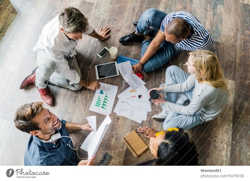 Happy business team sitting on floor discussing documents in loft office happiness happy discussion lofts paper papers offices office room office rooms