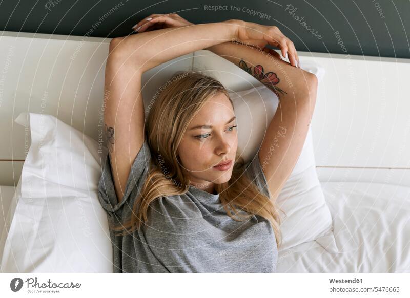 Serious blond young woman lying in bed laying down lie lying down serious earnest Seriousness austere females women blond hair blonde hair beds Adults grown-ups