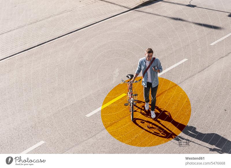 Man with wheeling bicycle using mobile phone while walking on road with gold colored circle color image colour image outdoors location shots outdoor shot