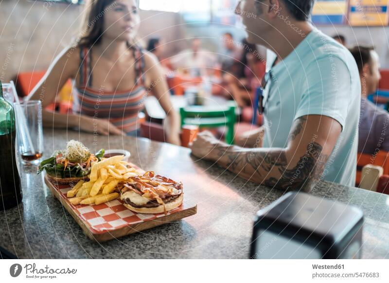 Hamburger and French fries on counter in a bar with couple socializing in background twosomes partnership couples hamburger looking eyeing French Fries