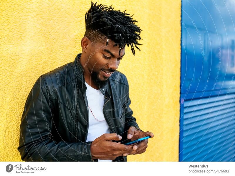 Close-up of mid adult man with locs using mobile phone while standing against wall color image colour image Spain leisure activity leisure activities free time