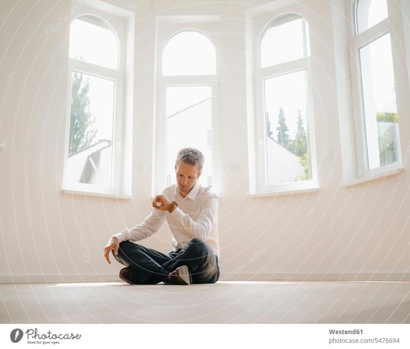 Businessman sitting on ground of his newly refurbished home, checking time new home new house Seated waiting Sitting On The Floor Sitting On Floor renovated