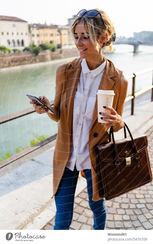 Smiling woman with coffee to go using smartphone in the city human human being human beings humans person persons caucasian appearance caucasian ethnicity