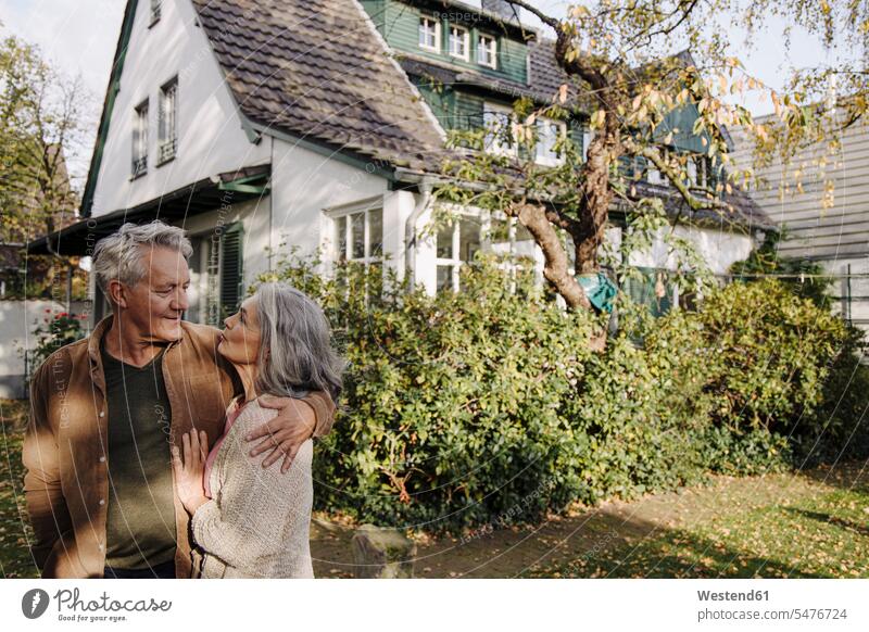 Senior couple in garden of their home in autumn relax relaxing smile embrace Embracement hug hugging seasons fall relaxation delight enjoyment Pleasant pleasure