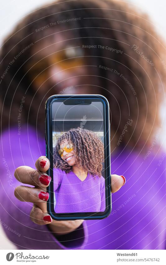 Afro woman showing selfie through mobile phone color image colour image outdoors location shots outdoor shot outdoor shots day daylight shot daylight shots