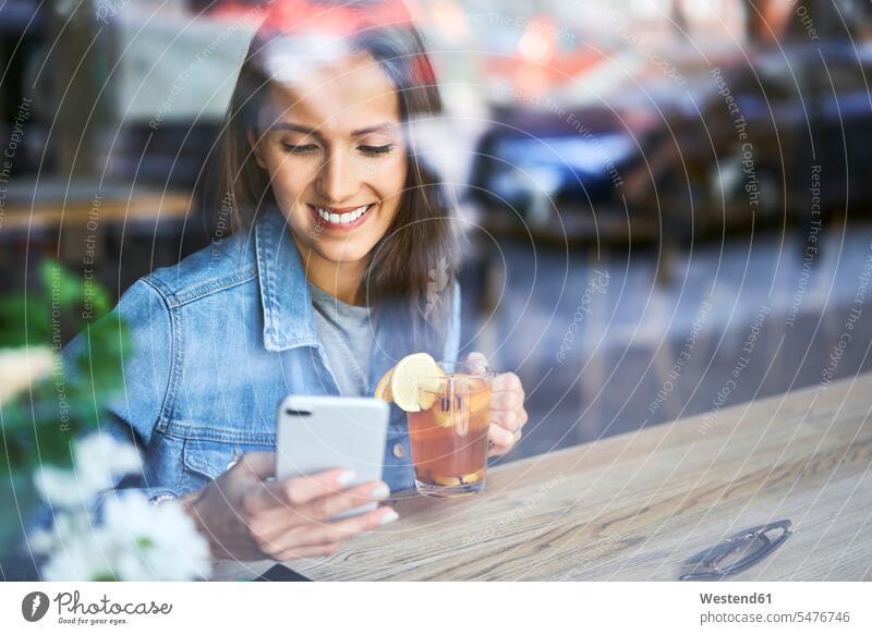 Smiling young woman using phone and drinking tea in cafe mobile phone mobiles mobile phones Cellphone cell phone cell phones Tea Teas smiling smile females