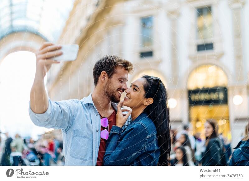 Happy young couple taking a selfie in the city, Milan, Italy touristic tourists telecommunication phones telephone telephones cell phone cell phones Cellphone