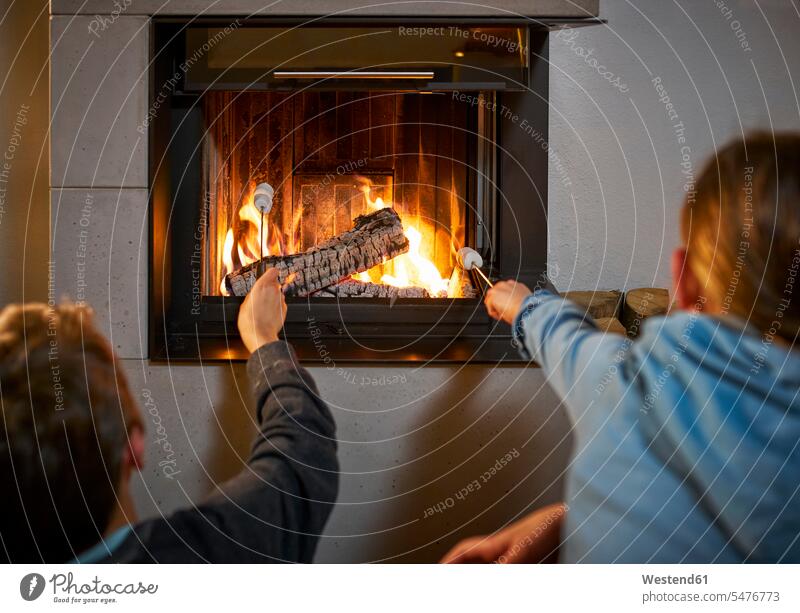 Back view of brother and sister with marshmallow Skewers in front of fire place relax relaxing barbecue Barbecuing grill grilling at home warm Athmospheric Mood