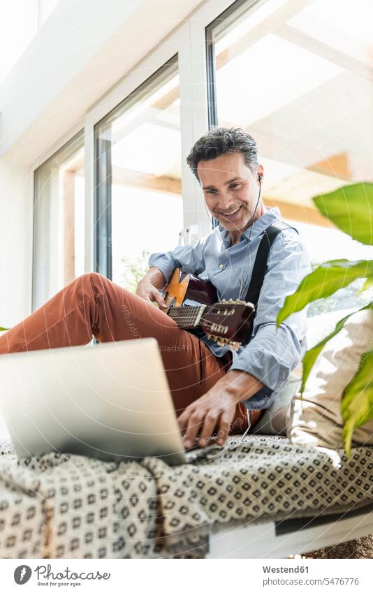 Mature man practising on the guitar, using laptop and earphones windows Instrument Instruments musical instruments stringed instruments guitars couches settee