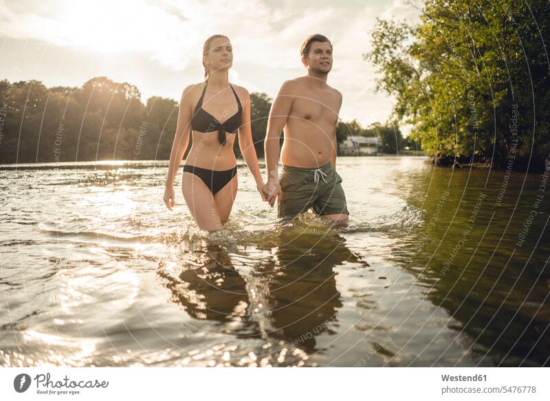 Young couple walking out of lake, holding hands swim wear bikinis relax relaxing go going summer time summertime summery happy Emotions Feeling Feelings
