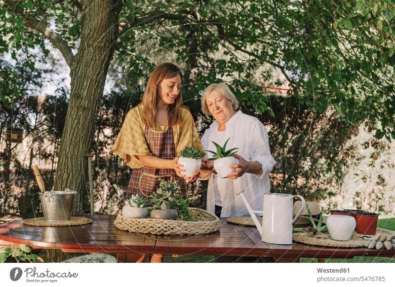 Mother and daughter holding potted plants while standing at table in yard color image colour image Spain leisure activity leisure activities free time