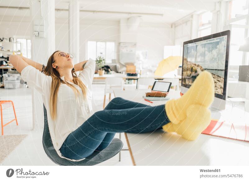 Young freelancer relaxing with feet up at desk in a loft freelancing desks lofts relaxation relaxed Table Tables glasses specs Eye Glasses spectacles Eyeglasses