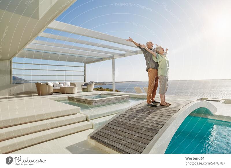 Carefree senior couple standing on bridge above a swimming pool at a luxury beach house touristic tourists relax relaxing relaxation enjoy enjoyment indulgence