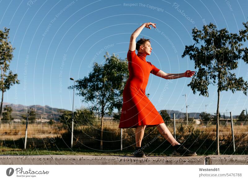 Non-binary male wearing red dress dancing on retaining wall color image colour image outdoors location shots outdoor shot outdoor shots day daylight shot