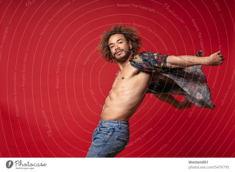 Young man wearing fully unbuttoned shirt dancing against red background color image colour image Spain Millennials Millennial Generation young adults Adults