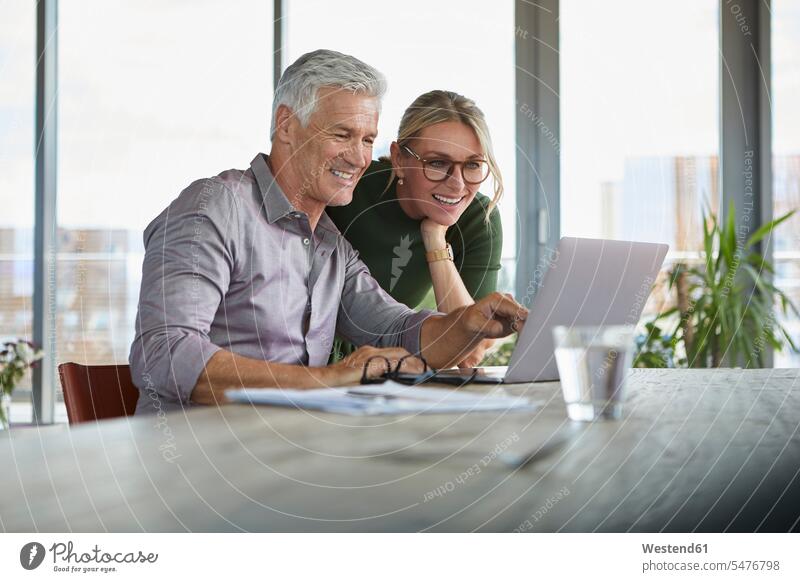 Smiling mature couple using laptop on table at home smiling smile twosomes partnership couples Table Tables Laptop Computers laptops notebook people persons
