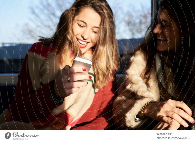 UK, London, two happy women in underground train using cell phone female friends mobile phone mobiles mobile phones Cellphone cell phones woman females