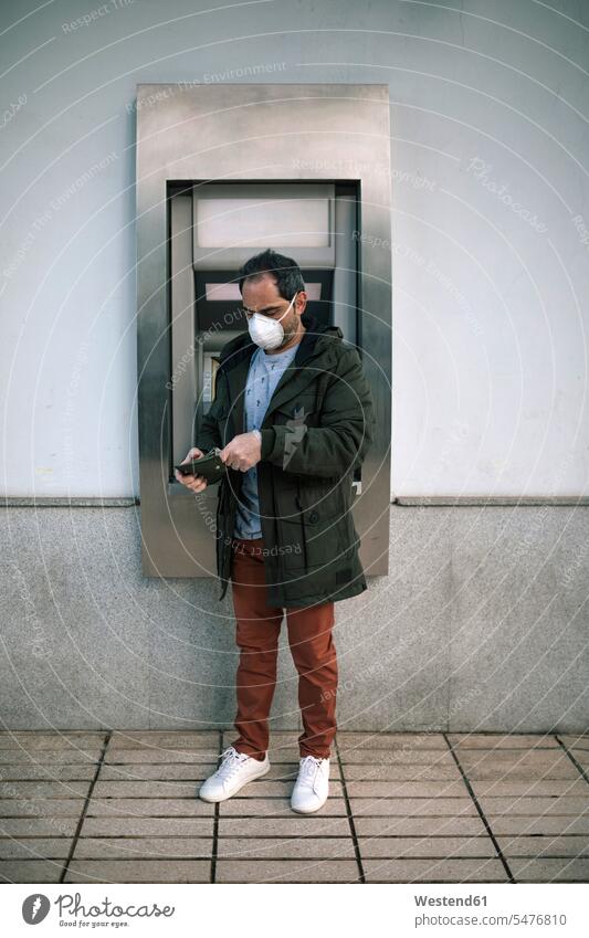 Man with protective mask standing in front of cash machine putting money in his purse purses protecting safe Safety secure location shot location shots outdoor