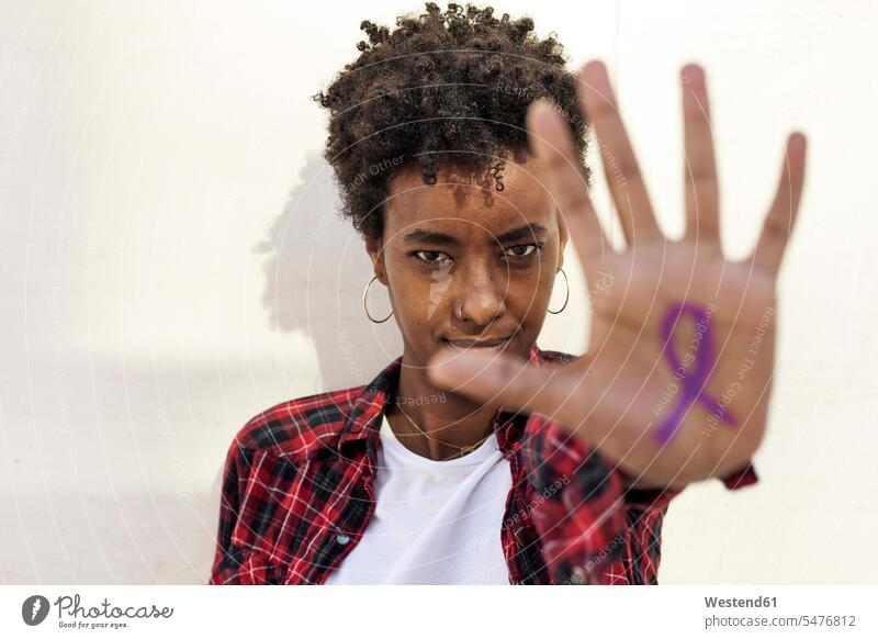 Confident young woman showing purple awareness symbol on palm against white wall during Womens Day color image colour image Spain outdoors location shots