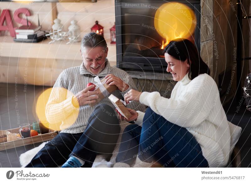 Happy mature couple at the fireplace unpacking gifts twosomes partnership couples present presents happiness happy relaxed relaxation sitting Seated people