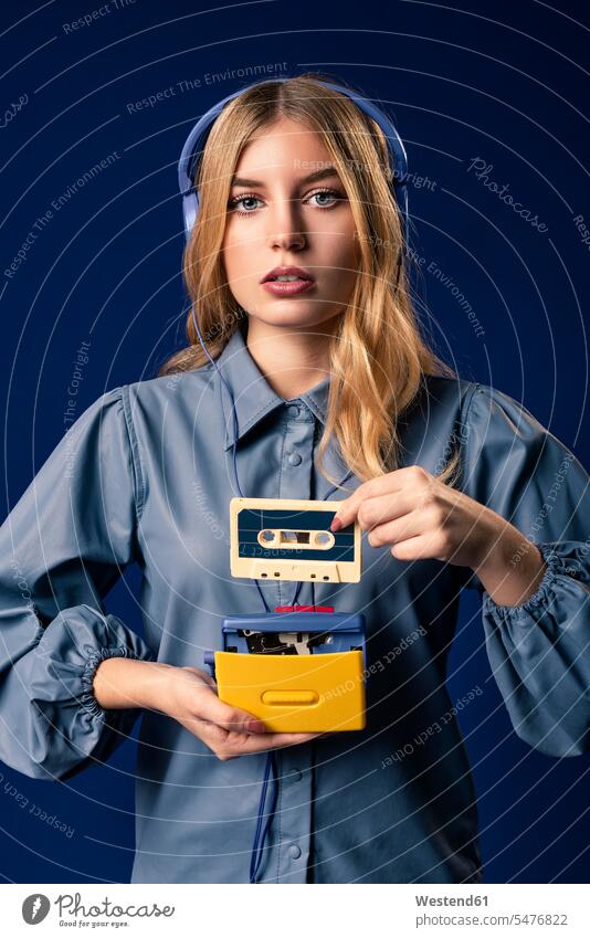 Young blond woman with walkman and headphones in front of blue background headset hold hear Retro retro revival Retro Styled Retro-Styled passionate free time