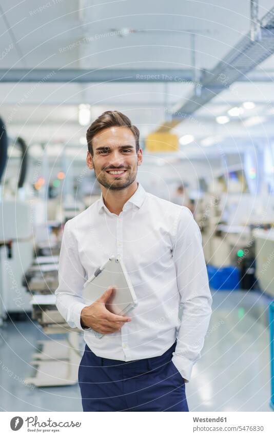 Smiling young businessman holding digital tablet while standing with hands in pockets at illuminated factory color image colour image indoors indoor shot