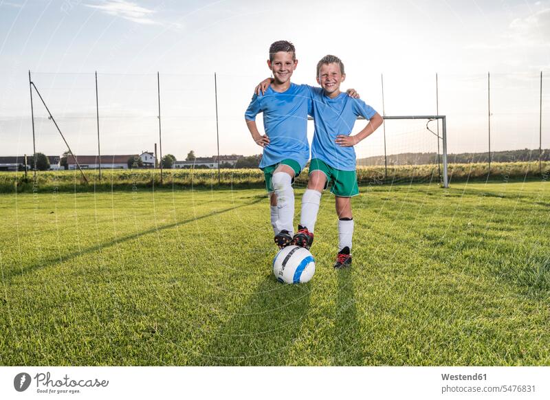 Smiling young football players embracing on football ground embrace Embracement hug hugging smiling smile footballers soccer players soccer pitch football pitch