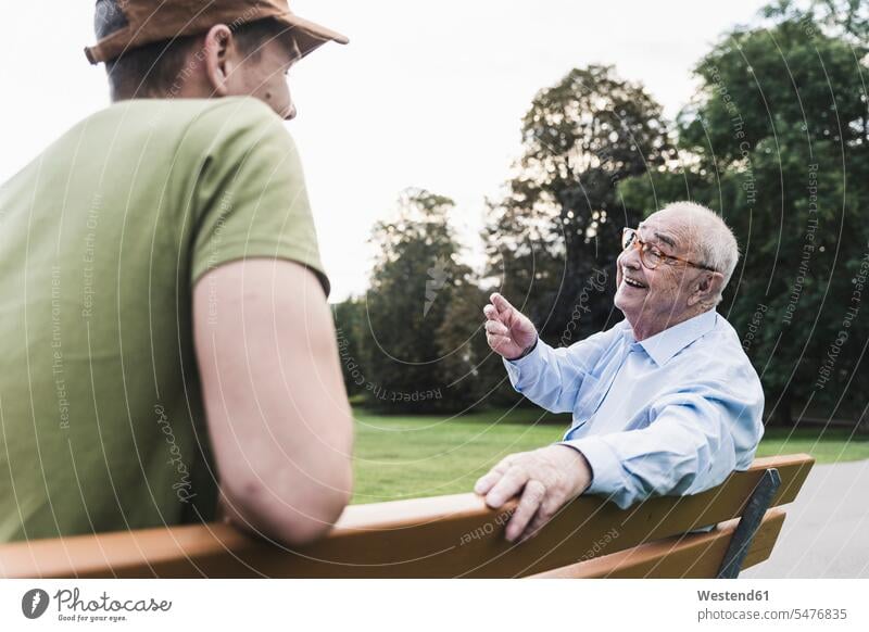 Happy senior man relaxing together with his grandson on a park bench generation Seated sit speak speaking talk relaxation delight enjoyment Pleasant pleasure