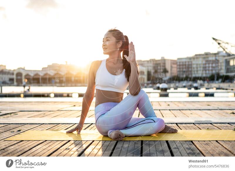Asian woman practicing yoga on a pier at harbour, half-spinal twist at sunset Seated sit in the evening Late Evening colored colorful coloured multi colored