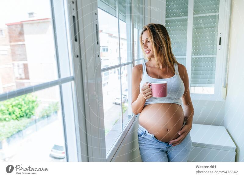Pregnant woman looking out of window holding mug windows females women mugs cup pregnant Pregnant Woman Adults grown-ups grownups adult people persons